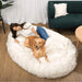 A woman enjoys relaxing with her dog on a White with Brown Accents Paw PupCloud™ Human-Size Faux Fur Memory Foam Dog Bed in a modern living room