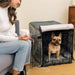 A woman sits next to a black wire crate with a grey interior, where a dog is comfortably resting, from the Paw Upgrade Your Dog Crate Kit - Charcoal Grey
