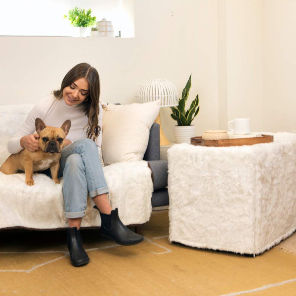 A woman sits on the couch with her dog, next to a black wire crate covered with white fabric, showcasing the Paw Upgrade Your Dog Crate Kit - Polar White