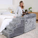 A woman stands next to the bed with a dog lying on the Paw Pet Bedside Sleeper Crate Kit & Stairs