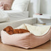 Blush Bowsers One Of A Kind Scoop Dog Bed shows a brown dog sleeping peacefully in a soft pink bed with a plush cream interior beside a neatly made bed