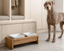 Bowsers Bamboo Artisan Wood Feeder double feeder sits beside a large gray dog, showing two white dog bowls on a low bamboo stand