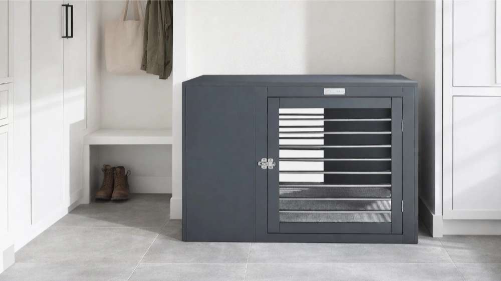 Bowsers Moderno Dog Crate is shown as a dark gray furniture-style crate placed neatly between white cabinets in a bright indoor room