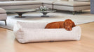 Brown dog relaxes comfortably inside a beige Bowsers Urban Lounger Dog Bed placed on a light wood floor in a modern living room