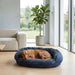 Brown dog relaxes on a plush navy blue Bowsers Crescent Reversible Dog Bed beside large windows in a bright modern living room