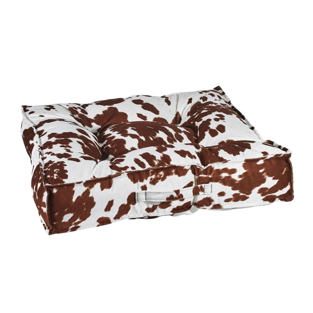 Durango Bowsers Piazza Dog Bed in brown-and-white cowhide print fabric features deep tufting and soft padded bolsters for comfort