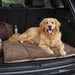 Golden retriever relaxes in the back of a car on a cushioned brown Bowsers Urban Home & Travel Mat, with a travel bag and bottle nearby
