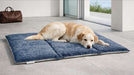 Light-colored dog lies comfortably on a soft, foldable blue Bowsers Urban Home & Travel Mat placed on a tiled floor near a glass door