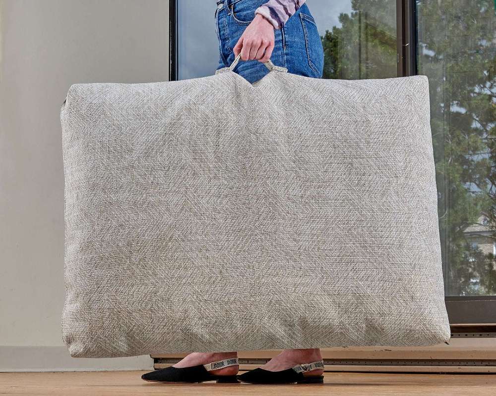 Person carries a large beige Bowsers Avenue Dog Bed with a built-in handle, showing its portable and lightweight design