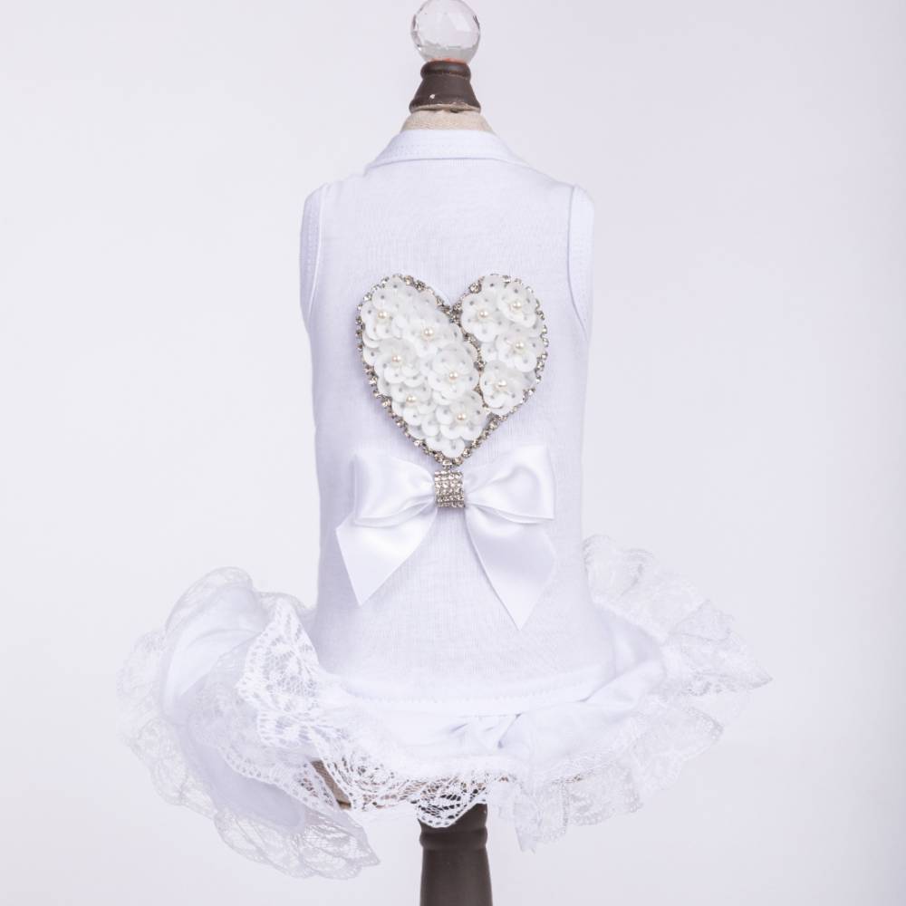 The image displays the Hello Doggie Endless Love Dog Dress, featuring a white dress with a heart-shaped floral design and a bow on the back, along with lace trim at the bottom