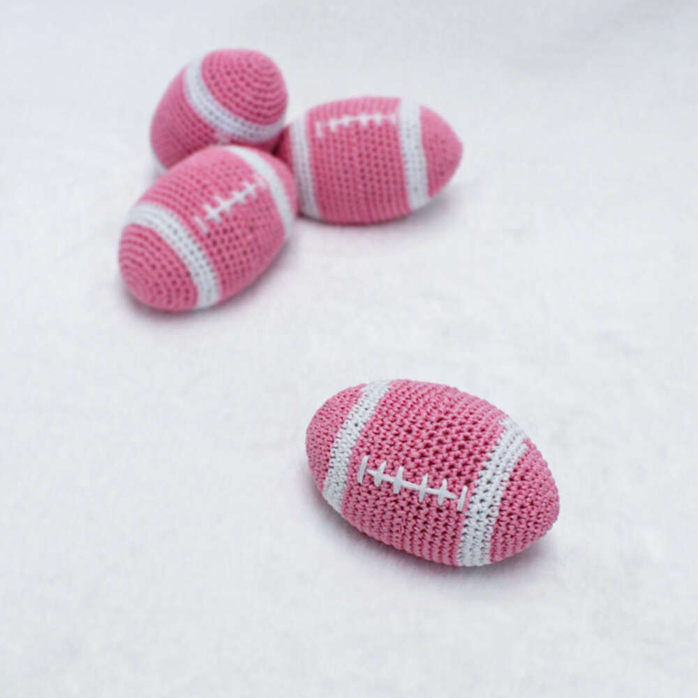 The image features four pink crocheted footballs, each labeled as a Hello Doggie Crochet Football Dog Toy, with one football in the foreground and three in the background