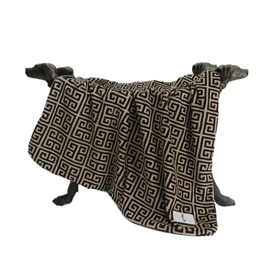 The image features the Hello Doggie Obsidian Dog Blanket, which is elegantly draped over dog-shaped supports, showcasing its black and tan Greek key pattern design