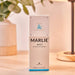 The image features the packaging of Paw Marlie Mist Pet Odor Eliminator Spray with Essential Oils - Fresh & Unscented placed on a wooden table next to a lamp and a plant