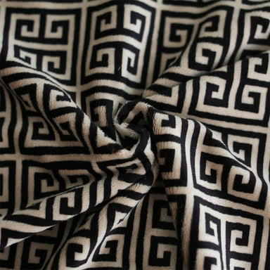The image is a close-up of the Hello Doggie Obsidian Dog Blanket, highlighting the intricate black and tan Greek key pattern on its soft, plush fabric