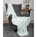 The image presents the Hello Doggie Whisper Dog Blanket in aqua color, beautifully arranged on a gray armchair for a soft and inviting look