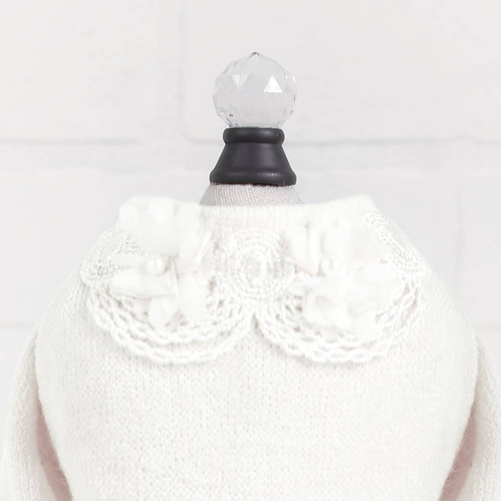 The image shows a detailed view of the collar on the Hello Doggie Sweet Magnolia Dog Sweater in cream, featuring delicate lace and flower embellishments
