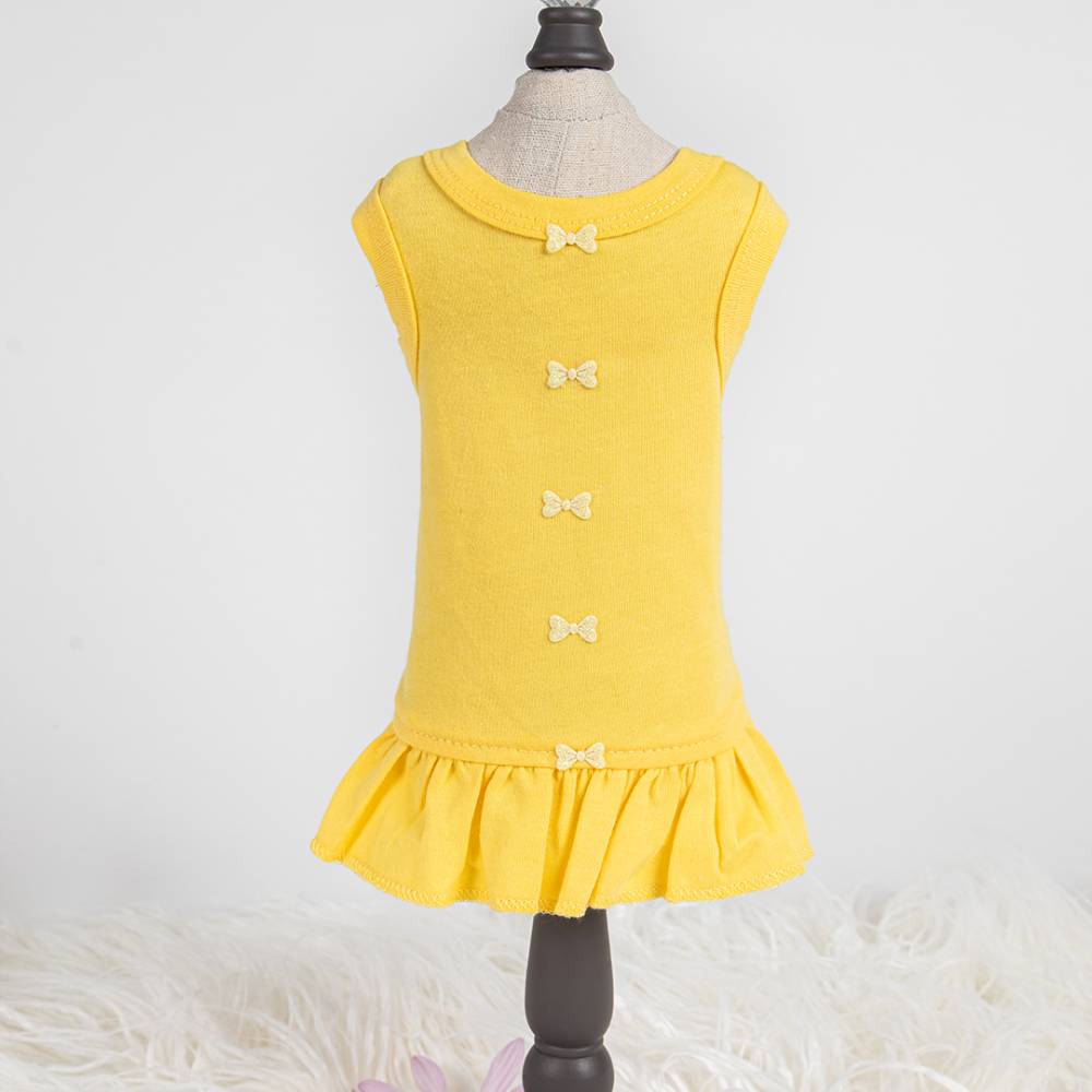The image shows a yellow Hello Doggie Candy Dog Dress on a mannequin with small decorative bows down the back and a ruffled hem