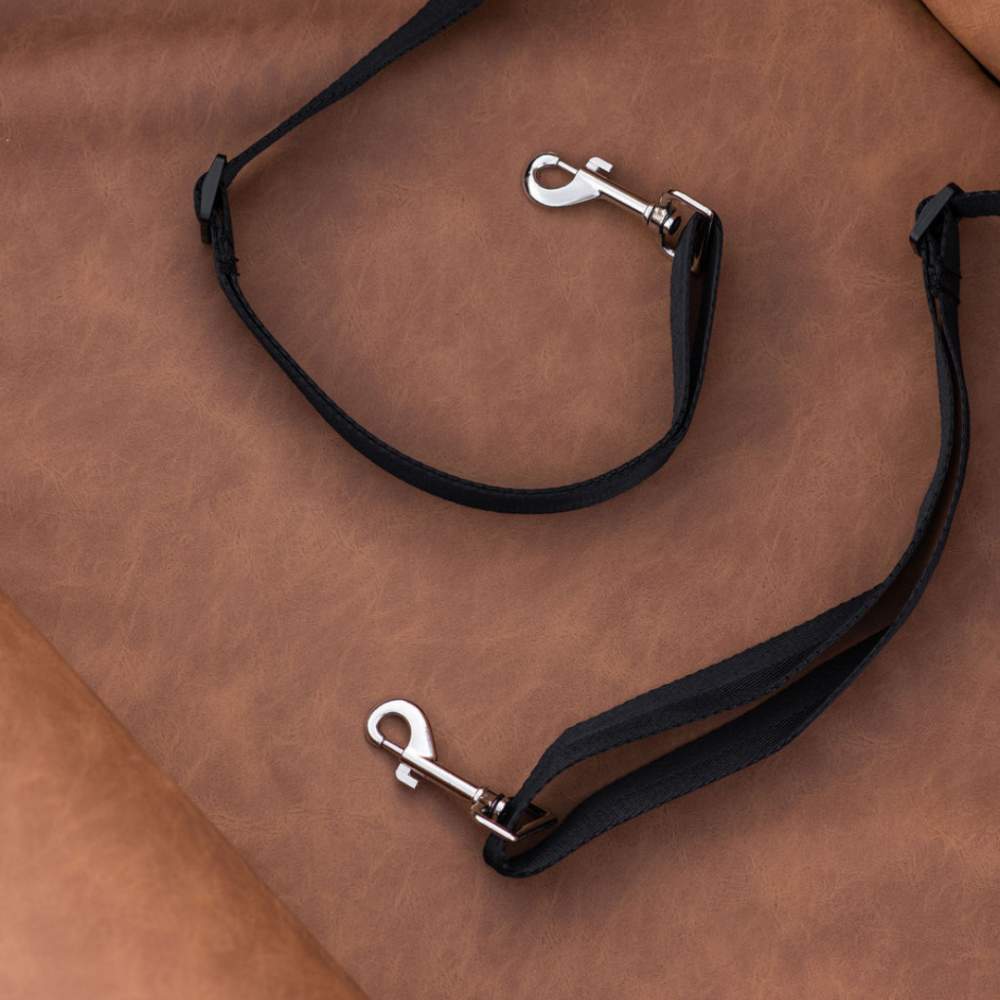 The image shows two black straps with metal clasps on a brown leather surface, part of the Paw PupProtector™ Faux Leather Memory Foam Dog Car Bed - Camel