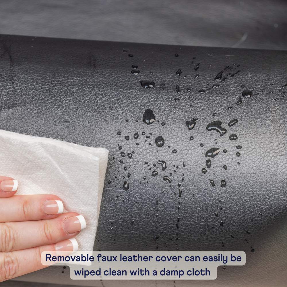 The removable faux leather cover of the Paw PupProtector™ Faux Leather Memory Foam Dog Car Bed - Black is shown being wiped clean with a damp cloth